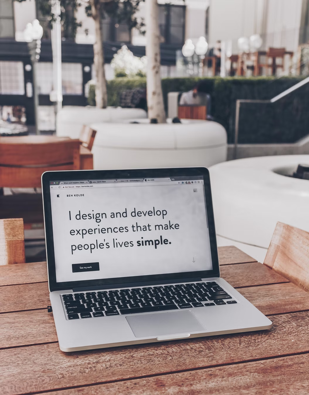 A computer on a table with a webpage open saying, "I design and develope experiences that make people's lives simple."